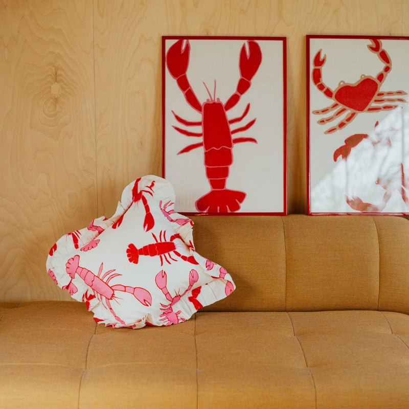Amuse La Bouche Lobster cushion on a brown sofa, next to framed lobster and crab tea towels.